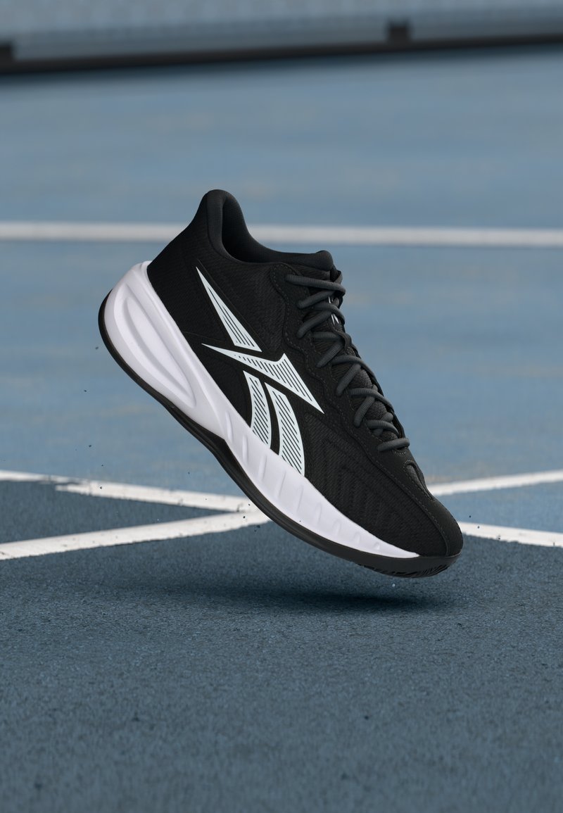 Zapatilla deportiva negra con parte superior texturizada, acentos en blanco y suela blanca acolchada. Presenta un diseño de cordones y una forma aerodinámica.