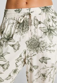 Bloemafdruk broeken in crème, met groene botanische ontwerpen. Elastische tailleband met trekkoord, ontworpen voor comfort. Zachte stoftextuur.