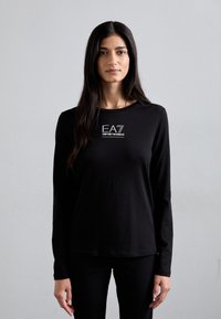 Zwarte lange mouwen shirt van zachte stof met een centraal wit logo ontwerp met de tekst "EA7" en "Emporio Armani". Eenvoudige, getailleerde vorm.