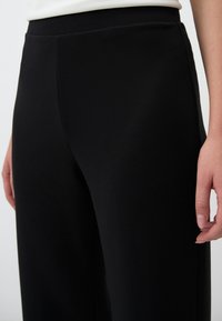 Pantaloni neri con una texture liscia e gambe larghe, dotati di una vita alta e tasche laterali. Nessun motivo o hardware visibile.