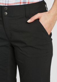 Pantaloni neri con due chiusure a bottone in metallo, caratterizzati da una texture liscia, tasca laterale e dettagli di cucitura sottili.