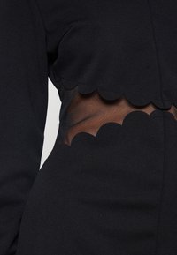 Vestito nero con un design a coste in vita e dettagli in rete trasparente, che enfatizzano la texture e il contrasto tra i materiali.