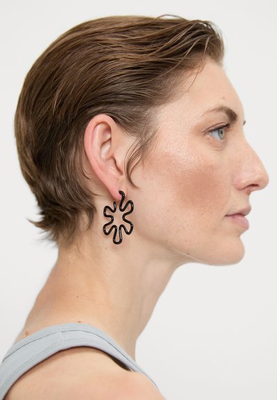 Schwarze Metal-Ohrstecker in einer fließenden, abstrakten Form, die einem Blütenblatt ähnelt, mit glänzendem Finish und leichtem Design.