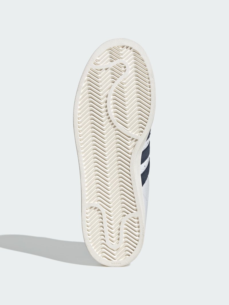 White sneaker sole with herringbone tread pattern, navy blue stripes on side, and shadow on light background.