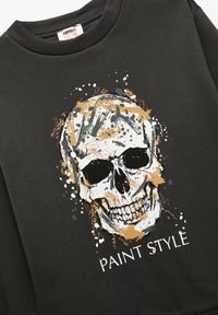 Sort sweatshirt med rund hals, udstyret med et grafisk motiv af et kranium prydet med hvide, gyldne og grønne malingsplamager samt teksten "PAINT STYLE."