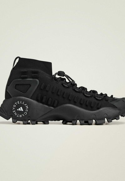 Le scarpe da esterno nere presentano una tomaia simile a un calzino, una rete strutturata e una suola in gomma prominente con profondi intagli e dettagli di branding.