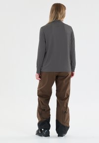 Harmaa pitkähihaisen paita, joka on yhdistetty ruskeisiin housuihin. Paidassa on säädettävät hihansuut ja mustat yksityiskohdat. Yksinkertainen ja toiminnallinen muotoilu ulkoiluun.