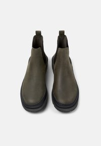 Botas de tobillo de cuero verde oliva con paneles laterales elásticos, puntera redonda y una suela de goma negra gruesa. Textura suave con un detalle mínimo.