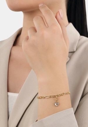 Braccialetto in oro con un ciondolo a forma di cuore, caratterizzato da una finitura lucida e link di dimensioni diverse, indossato su un polso.