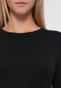 Pull en maille côtelée noir avec un col rond et une texture douce, raccourci au niveau des épaules, sans motifs ni accents visibles.
