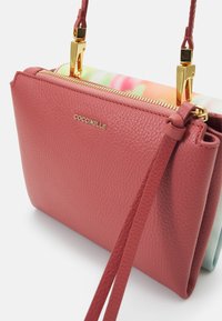 Petit sac à main en cuir rose texturé avec fermeture éclair dorée et garnitures, panneau en tissu floral et bandoulière amovible.