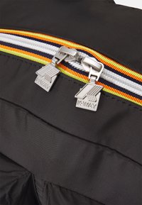 Giacca nera con zip multi-strisce caratterizzata da dettagli arancioni, verdi e blu; hardware metallico e tessuto testurizzato. Visibile il marchio K-Way.