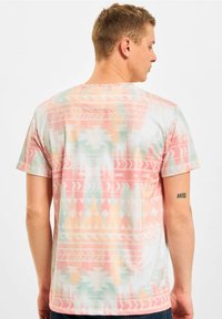 Short-sleeve graphic tee in pastel colors with geometric patterns, featuring a relaxed fit and soft fabric. Accents include horizontal stripes.