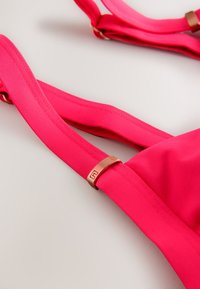 Élénk rózsaszín melltartó sima, rugalmas pántokkal és egy fémszerű díszítéssel a kapocs közelében. Minimalista kialakítású és puha tapintású.