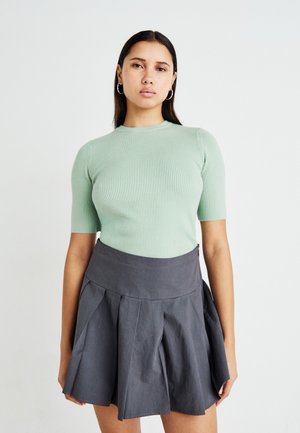 Un haut vert menthe à manches courtes à côtes associé à une jupe plissée grise foncée. Le haut présente un col rond et une silhouette ajustée.