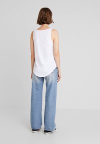 Top blanc sans manches associé à un jean large bleu clair. Les jeans ont un effet délavé et sont associés à des baskets noires.