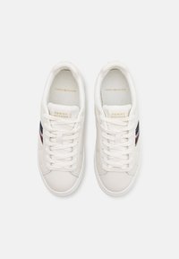 Paire de baskets basses blanches avec lacets à l'avant, languette de marque et bandes latérales bleu marine, rouge et blanc, vues de dessus sur fond blanc.
