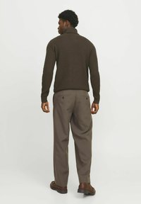 Maglione di lana marrone con colletto alto, abbinato a pantaloni grigi larghi e scarpe marroni. Design semplice senza motivi visibili.