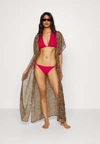Conjunto de biquíni vermelho com um top de pescoço halter e laterais ajustáveis, acompanhado de um vestido cobridor transparente com padrão de leopardo, apresentando um tecido leve.