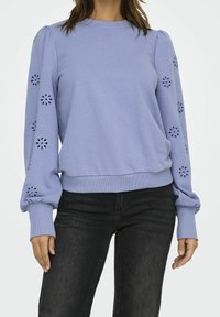 Ljuslila långärmad topp med blommig utskuren broderi på ärmarna, puffiga handleder, kombinerad med svarta jeans.