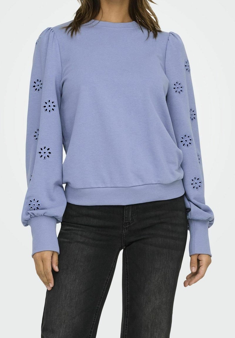 Ljuslila långärmad topp med blommig utskuren broderi på ärmarna, puffiga handleder, kombinerad med svarta jeans.