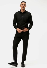 Schwarzes langärmeliges Hemd mit einem knöpfbaren Design, passende Hose und polierte schwarze Schuhe. Verfügt über eine Brusttasche und eine taillierte Passform.