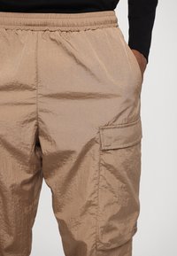 Beiga lätta cargobyxor med elastisk midja, sidoficka och lätt lyster. Texturerad tyg med avslappnad passform.