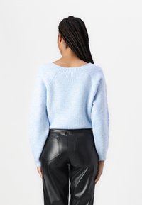 Maglione azzurro chiaro a maglia testurizzata con scollatura ampia e maniche lunghe a palloncino, abbinato a pantaloni neri in ecopelle a vita alta.