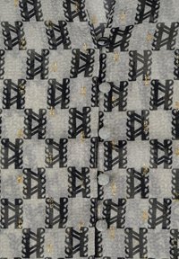 Transparent grå blus med ett upprepat svart abstrakt mönster och guldaccenter, runda knappar och en strukturerad yta.