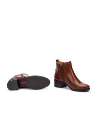 Bruna läderankelboots med låg klack, sidodragkedja och texturerade detaljer på sidorna. Gummisula med mönster synlig från undersidan.