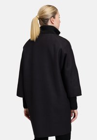 Czarny, oversize płaszcz z wysokim, ryflowanym kołnierzem i krótkimi rękawami, charakteryzujący się gładką teksturą i minimalistycznym wzornictwem.