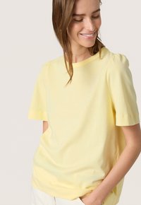 Tricou scurt cu mânecă scurtă de culoare galben deschis, cu decolteu rotund și detaliu cu umeri bufantați, fabricat dintr-un material moale, cu o croială lejeră, fără modele vizibile.