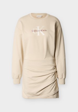 Bēšas krāsas sporta kleita ar garām piedurknēm, apaļu kakla izgriezumu, savilktām detaļām sānos un priekšpusē sarkanā un baltā krāsā izšūtu logotipu "Calvin Klein". Mīksts audums.