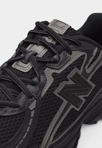 Gros plan d'une basket noire New Balance avec des accents gris, un tissu en maille et des lacets passés dans des œillets sur le dessus.