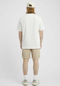 T-shirt blanche à manches courtes, coupe décontractée, associée à un short beige retroussé. Portée avec des baskets blanches et grises et une casquette légère.