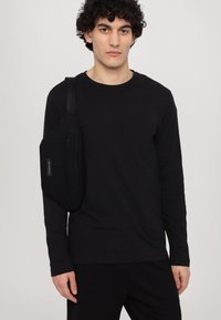 Camisa negra de manga larga con cuello redondo, combinada con pantalones negros. Se lleva un pequeño bolso cruzado negro en el hombro izquierdo.