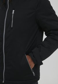 Black insulated jacket featuring a central zipper, side pockets with grey accents, and a textured material for warmth and comfort.