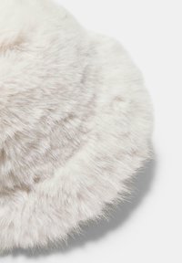 Cuscino rotondo in morbida pelliccia sintetica bianca, caratterizzato da una texture morbida e pelosa e una forma leggermente appiattita con lunghe e soffici fibre lungo il bordo.