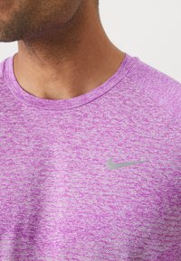 Lila meliertes Sport-T-Shirt mit rundem Hals und kurzen Ärmeln. Verfügt über ein kleines silbernes Nike-Logo auf der linken Brustseite.