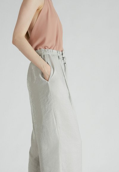 Jasnoróżowa bluzka bez rękawów o luźnym kroju, zestawiona z jasnoszarymi, szerokimi spodniami z talią na sznurku i bocznymi kieszeniami.