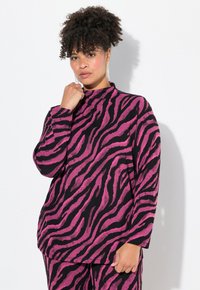 Långärmad topp i rosa och svart zebramönster, hög hals, mjuk textur, lös passform, med en person som poserar mot en enfärgad bakgrund.