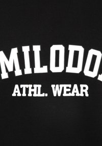 Sudadera negra con texto blanco en negrita que dice "MILODO. ATHL. WEAR." La tela parece suave, con una textura lisa y un diseño casual.