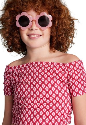 Occhiali da sole a forma di fiore rosa con lenti scure, indossati da un bambino che indossa una maglietta scollata rossa e bianca a rombi con dettagli arricciati.