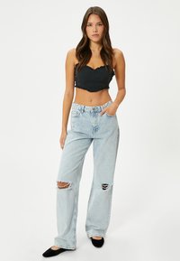 Zwarte crop top met geschulpte randen, gecombineerd met lichtblauwe baggy jeans met grote kniebars en rafelige zoom. Zwarte flats maken de look af.