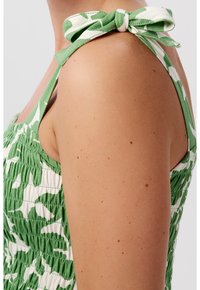 Grön och vit mönstrad ärmlös topp med smockad textur, med en knytning vid axeln och en figurnära design.