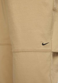 Beżowe sportowe szorty z lekkiego materiału, z czarnym logo Nike, płaskimi szwami i gładką fakturą.