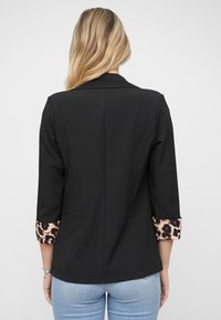 Svart blazer med trekvart lange ermer, med leopardmønstrede mansjetter. Enkel design, glatt tekstur og skreddersydd passform.