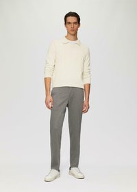 Jasno-kremowy sweter z kołnierzykiem, zestawiony z szarymi, dopasowanymi spodniami dresowymi i białymi sneakersami. Ubranie wyróżnia się casualowym, minimalistycznym stylem.