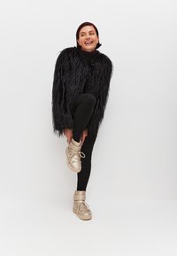 Cappotto in pelliccia sintetica nera e pelosa, leggings neri e sneakers alte in oro metallico con lacci e cinghie, posizionati su uno sfondo neutro.