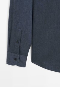 Dark blue long-sleeve button-up shirt with a textured fabric, featuring a pointed cuff and a rounded hem, showcasing two buttons on the cuff.